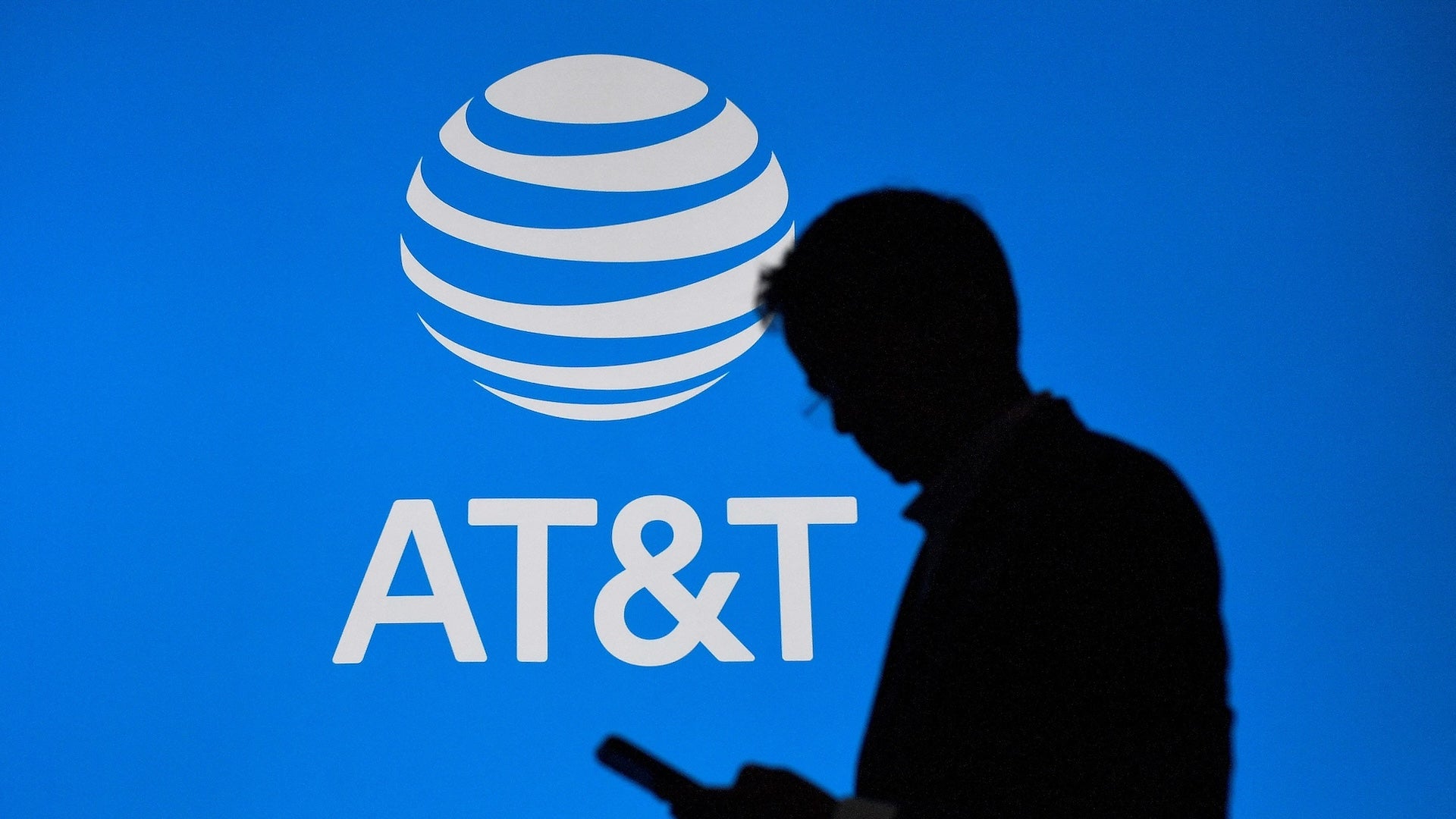 A person looking at their phone in front of an AT&T logo