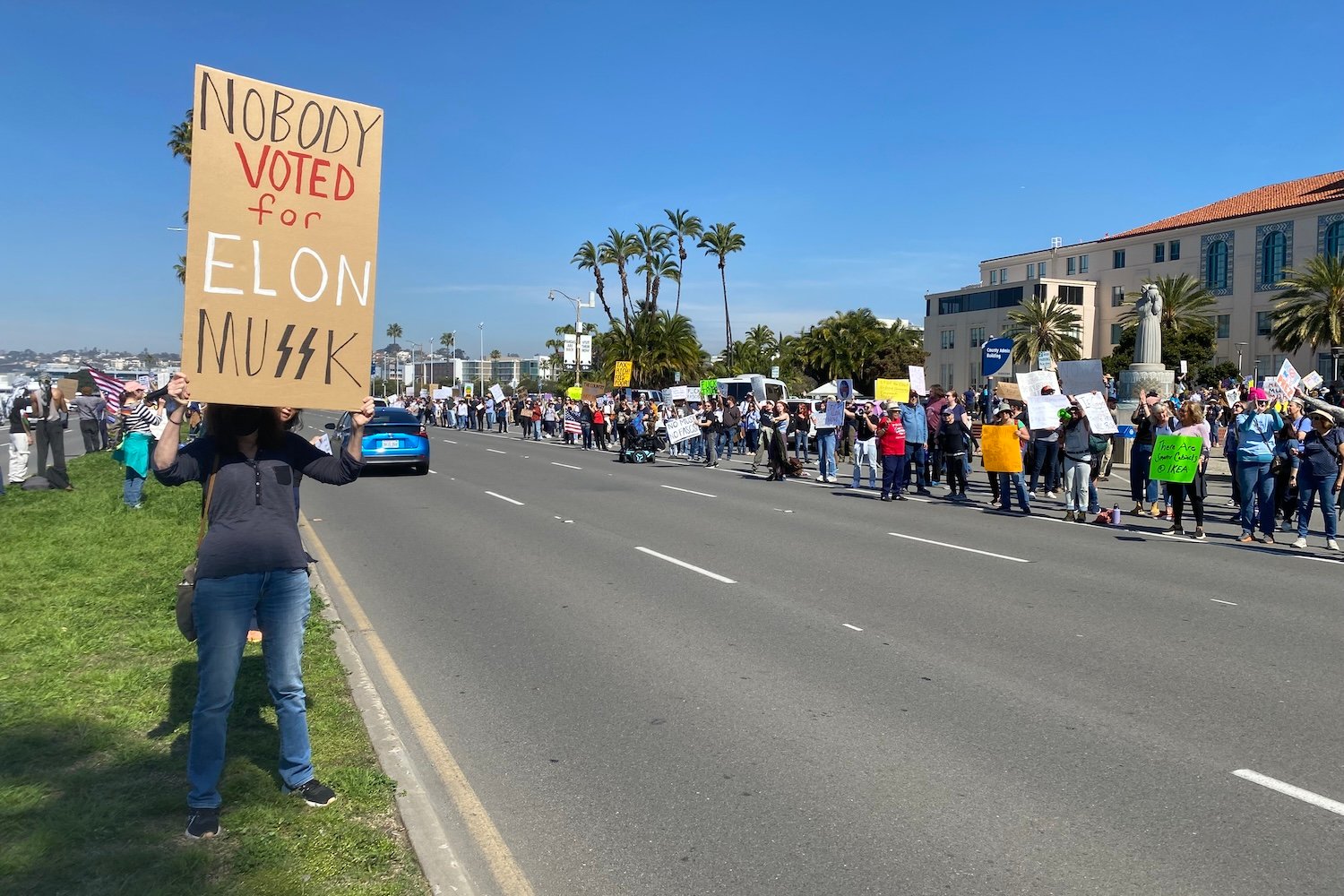 Protesters hold signs at a protest against Elon Musk and Donald Trump on Feb. 18, 2025 San Diego, California.