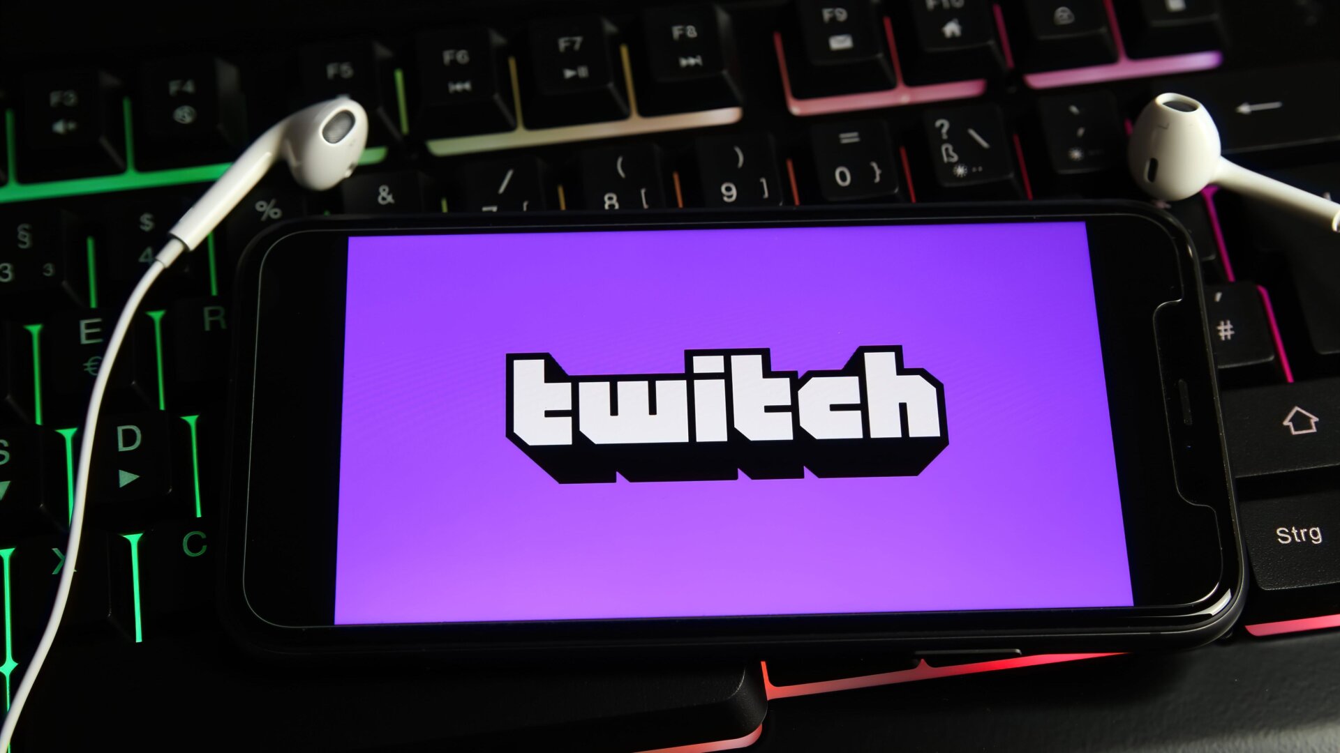 Twitch logo appears on a phone screen that sits above an illuminated keyboard.