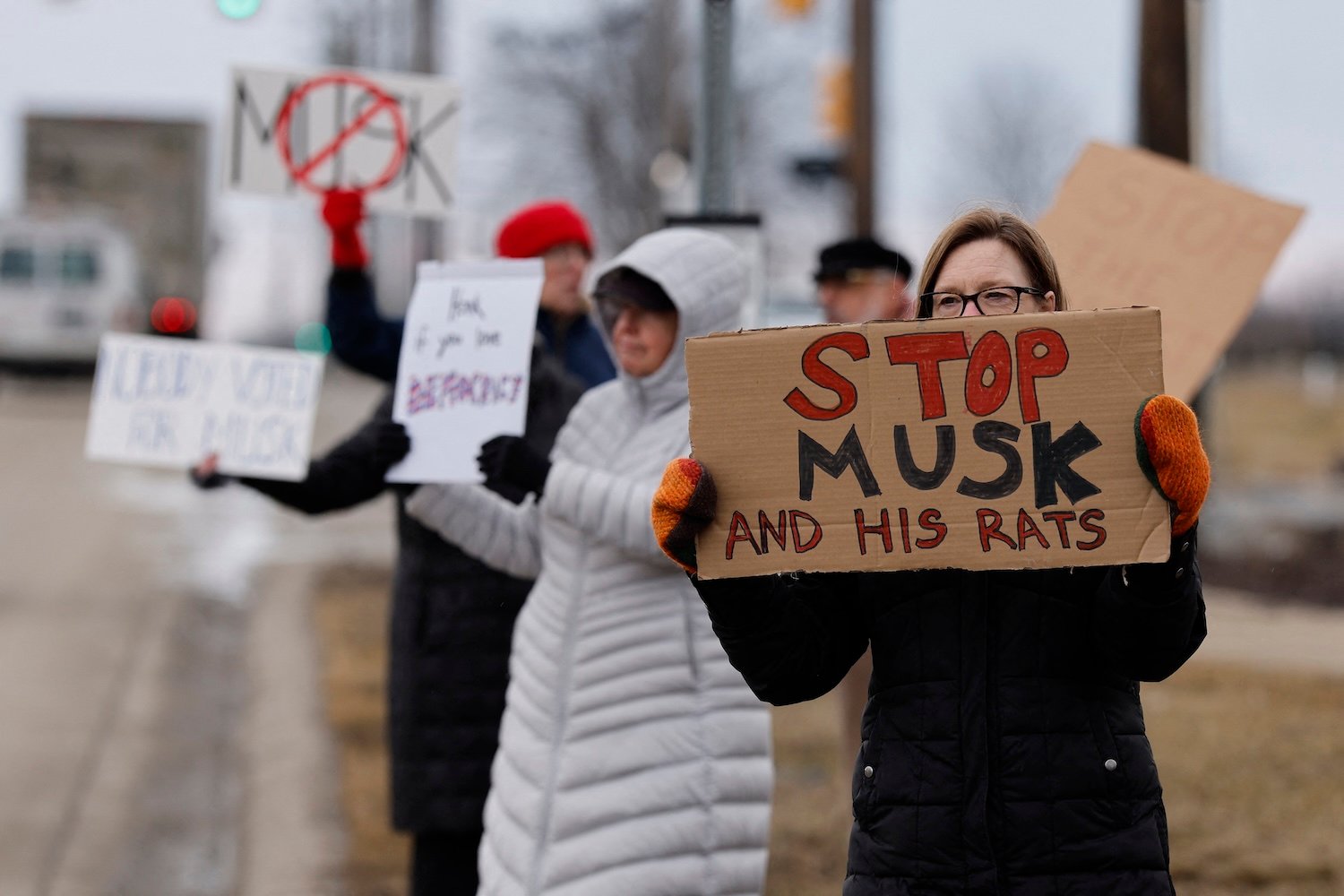 People hold signs during a protest against Elon Musk outside of a Tesla dealership in West Bloomfield, Michigan, on February 27, 2025.