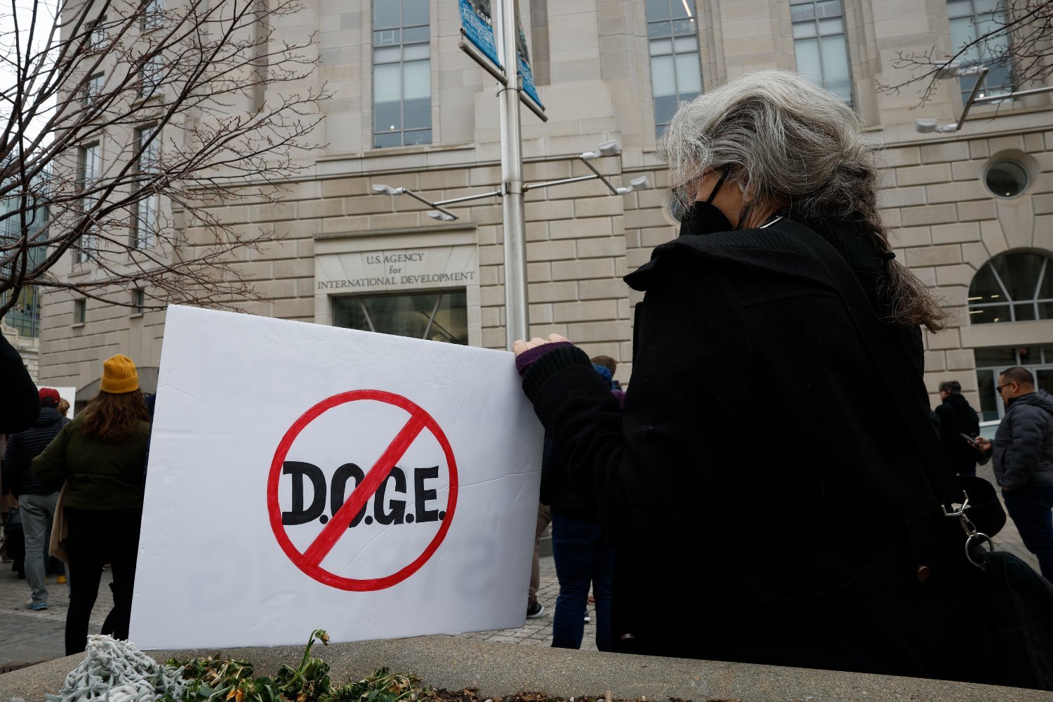 A protester outside of the U.S. Agency for International Development (USAID) headquarters holds a sign with an anti-DOGE message