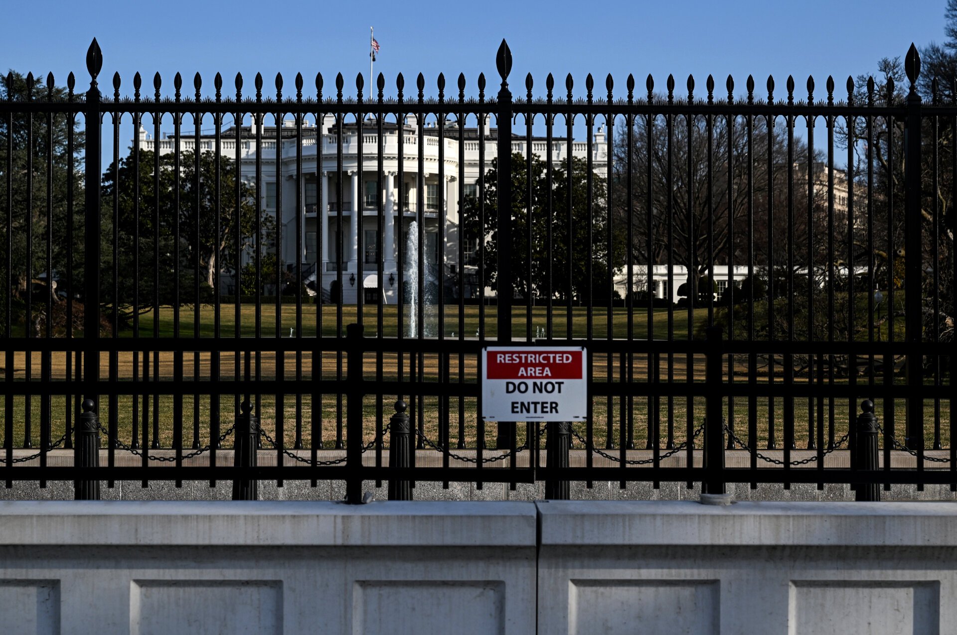 A photo of the outside of the White House and the gate surrounding it. A sign reads "Restricted Area: Do Not Enter."